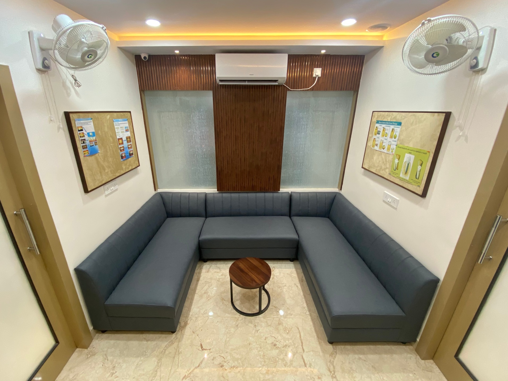 U-shaped grey sofa waiting lounge with patient information boards at OroCare Dental Clinic, Mukundapur