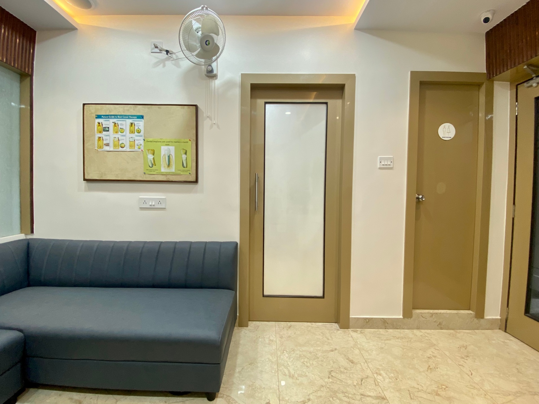 Waiting corridor with grey sofa and restroom access at OroCare Dental Clinic, Mukundapur