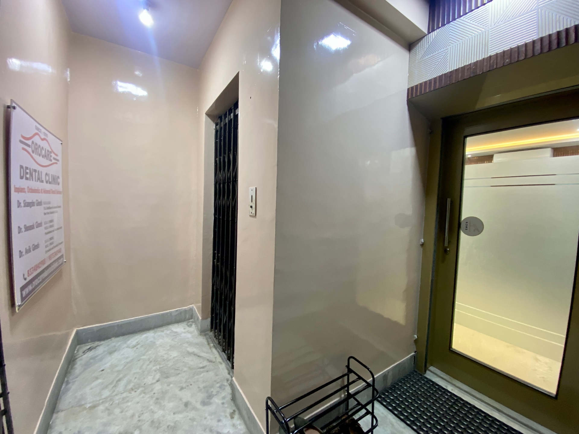Ground-floor entrance corridor with OroCare Dental Clinic signboard listing Dr. Sitangshu, Dr. Shounak and Dr. Avik Ghosh, Mukundapur